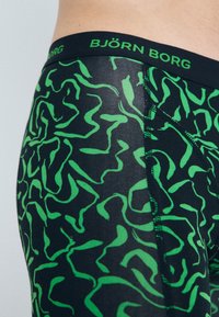 Black boxer briefs featuring a green abstract wavy pattern. Elastic waistband displays "BJÖRN BORG" in green text. Smooth, stretchy fabric.