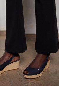 Sandali a zeppa navy con design open toe, tomaia in tela, piattaforma intrecciata e cinturino alla caviglia, con un piccolo logo decorativo.