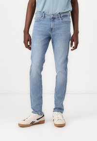 Világoskék denim farmernadrág, slim fit szabással, finom kopásokkal, öt zsebes kialakítással és normál derékkal, elöl gombos záródással.