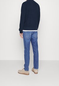 Felpa blu navy a maniche lunghe, abbinata a jeans di denim blu. Calzature di un beige chiaro con tomaia testurizzata e suola in gomma.