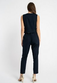 Czarna granatowa koszulka bez rękawów o dopasowanym kroju, zestawiona z dopasowanymi spodniami o smukłej sylwetce i złotymi sandałami na obcasie.