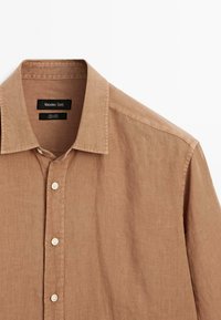 Chemise en lin marron avec un col, présentant une patte de boutonnage à l'avant et des boutons blancs. L'étiquette indique "Massimo Dutti" avec les instructions d'entretien à l'intérieur.