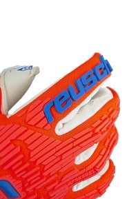 Gant de gardien de but orange avec une texture antidérapante, des doigts rembourrés blancs et un logo Reusch bleu sur une large sangle. Motifs notables sur la paume.
