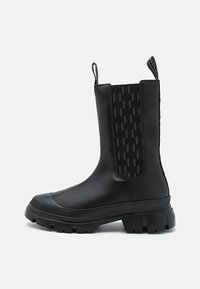 Bottines noires, avec un extérieur en cuir lisse, des panneaux latéraux en élastique texturé, et une semelle en caoutchouc épaisse avec des reliefs profonds.