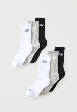 Τρία ζευγάρια κάλτσες New Balance σε λευκό, γκρι και μαύρο, κάθε ζευγάρι με το λογότυπο της εταιρείας κοντά στη μανσέτα.