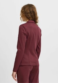 Burgundy sovitettu bleiseri kauluksella, pitkähihaisilla hihoilla ja muotoilluilla saumoilla. Valmistettu sileästä, venyvästä kankaasta, yhdistettynä yhteensopiviin housuihin.