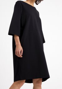 Czarna sukienka o obniżonej talii z trzema czwarte rękawami, wykonana z gładkiego materiału, z okrągłym dekoltem i luźnym krojem.