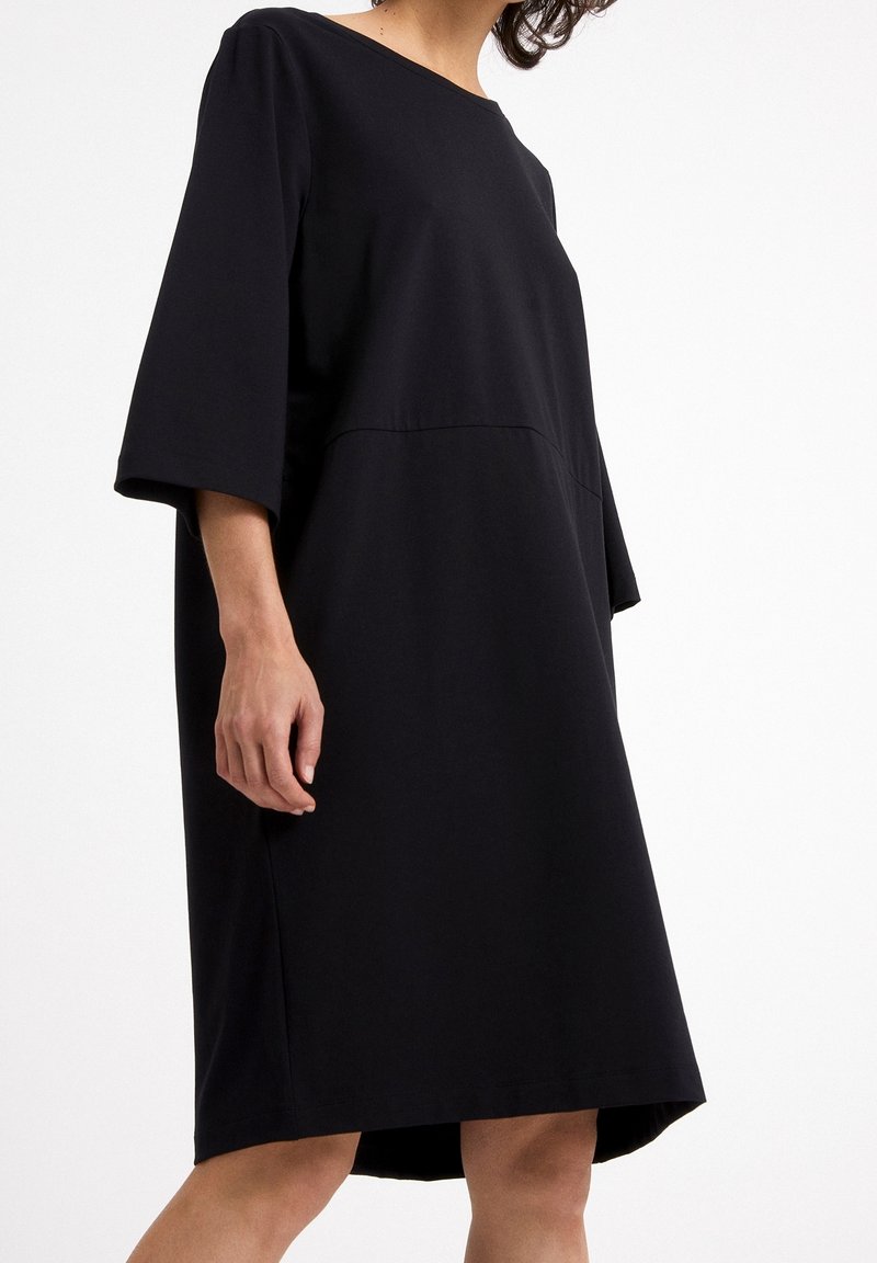 Czarna sukienka o obniżonej talii z trzema czwarte rękawami, wykonana z gładkiego materiału, z okrągłym dekoltem i luźnym krojem.