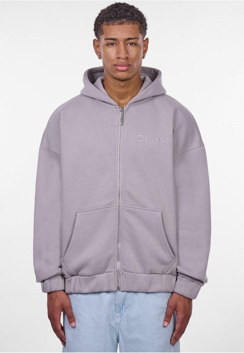 Hellgraue Zip-Hoodie mit weitem Schnitt, großen Fronttaschen und weichem Material. Verfügt über ein dezentes, auf die Brust gesticktes Logo.