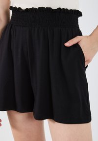 Shorts noirs avec une taille smockée et un ourlet froncé, dotés de poches latérales et d'un tissu léger et doux pour plus de confort.