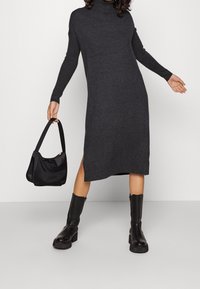 Czarna, dzianinowa sukienka w odcieniu ciemnoszarym z wysokim kołnierzem i długimi rękawami, z bocznymi rozcięciami. Połączona z czarną torebką i czarnymi butami na platformie.