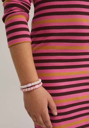 Gestreepte ribbed jurk in roze, bruin en geel; hand versierd met drie gevlochten armbanden in pastelkleuren en kralen.