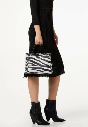 Borsa con stampa zebrate in bianco e nero, dotata di manici robusti e design strutturato. Abbinata a un vestito nero a coste e stivaletti alla caviglia.