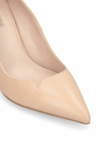 Scarpa con tacco alto in pelle beige con punta affusolata e dettagli a ondina. Texture liscia, design aderente e silhouette slanciata per un aspetto elegante.