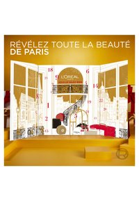 Le calendrier de l'Avent L'Oréal Paris présente un design doré et blanc avec une architecture parisienne illustrée, des chiffres audacieux et des accents rouges.
