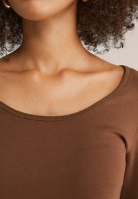 Braunes, kurzärmliges Oberteil mit weitem Ausschnitt und subtiler gerippter Textur sowie kontrastierenden Nähten entlang der Kanten.