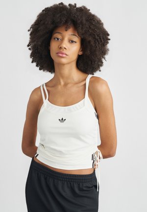Débardeur de sport blanc avec liens latéraux réglables, doté d'un col rond et du logo Adidas noir. Porté avec un short noir à cordon de serrage.