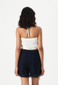 Hvit strikket bandeau-top med ribbestruktur, parret med marineblå blonde-shorts med bølgete kanter og elastisk liv.