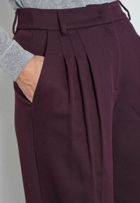 Burgundia pleeditud püksid tekstureeritud kangast, laia lõikega, küljetaskutega ja vöökohaga, millel on vöölõngad.