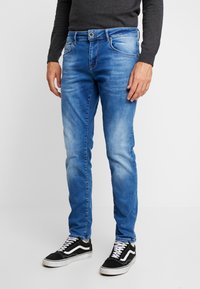 Lyseblå denimjeans med rette ben, fem lommer og subtil bleking på lårene, parret med svarte sneakers.