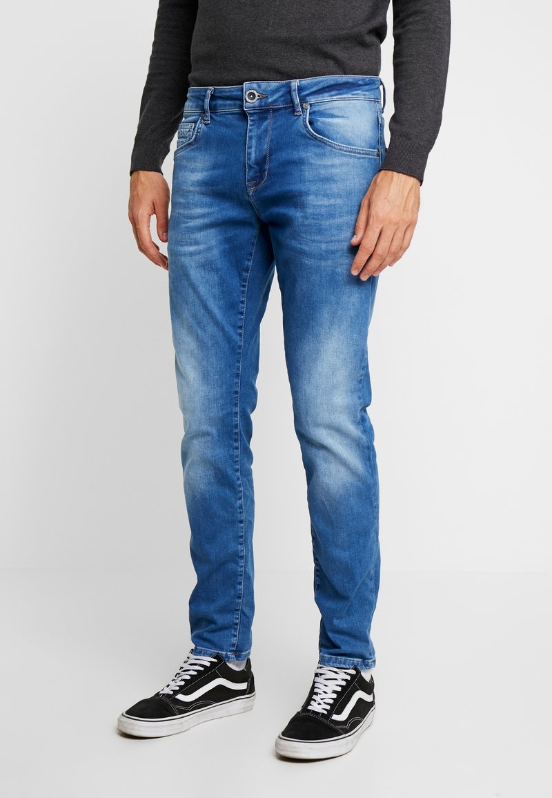 Lyseblå denimjeans med rette ben, fem lommer og subtil bleking på lårene, parret med svarte sneakers.
