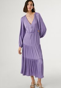Robe midi lavande avec un décolleté en V profond, de longues manches amples, des boutons sur le devant et des détails de ruffles superposés à l'ourlet. Tissu lisse.