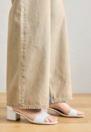 Lyseblå blockhælede sandaler med to brede stropper. Båret med beige vide bukser, der fremhæver skodesignet mod stofets struktur.