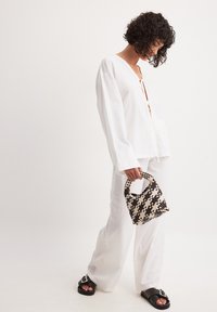 Camicia bianca, morbida e a maniche lunghe con un nodo frontale, abbinata a pantaloni coordinati e a una piccola borsa tessuta in bianco e nero.
