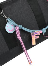 Sac en tissu noir avec cordon bleu et accessoires en porte-clés comprenant un pompon tressé rose-violet, une étiquette avec un visage souriant et un charm en forme de lettre F irisé.