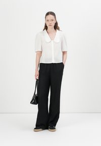 White, short-sleeved blouse with a large collar, paired with black, wide-leg trousers and black sneakers. Model holds a small black handbag.