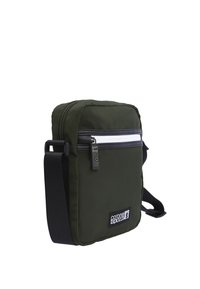 Bolso bandolera verde de nailon con un bolsillo con cremallera en la parte delantera, correa negra ajustable, textura suave y detalles en cremallera blanca. Parche con el logo en la parte delantera.