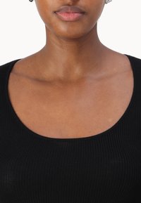 Svart ribbet topp med scoop-hals, myk tekstur og tettsittende design, som fremhever skuldrene og kragebeinsområdet.