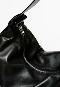 Zwarte leren tas met een gladde textuur, voorzien van een metalen rits en een slouchy design. Kenmerkende afgeronde handgreep die verstelbaar is voor gemakkelijk dragen.