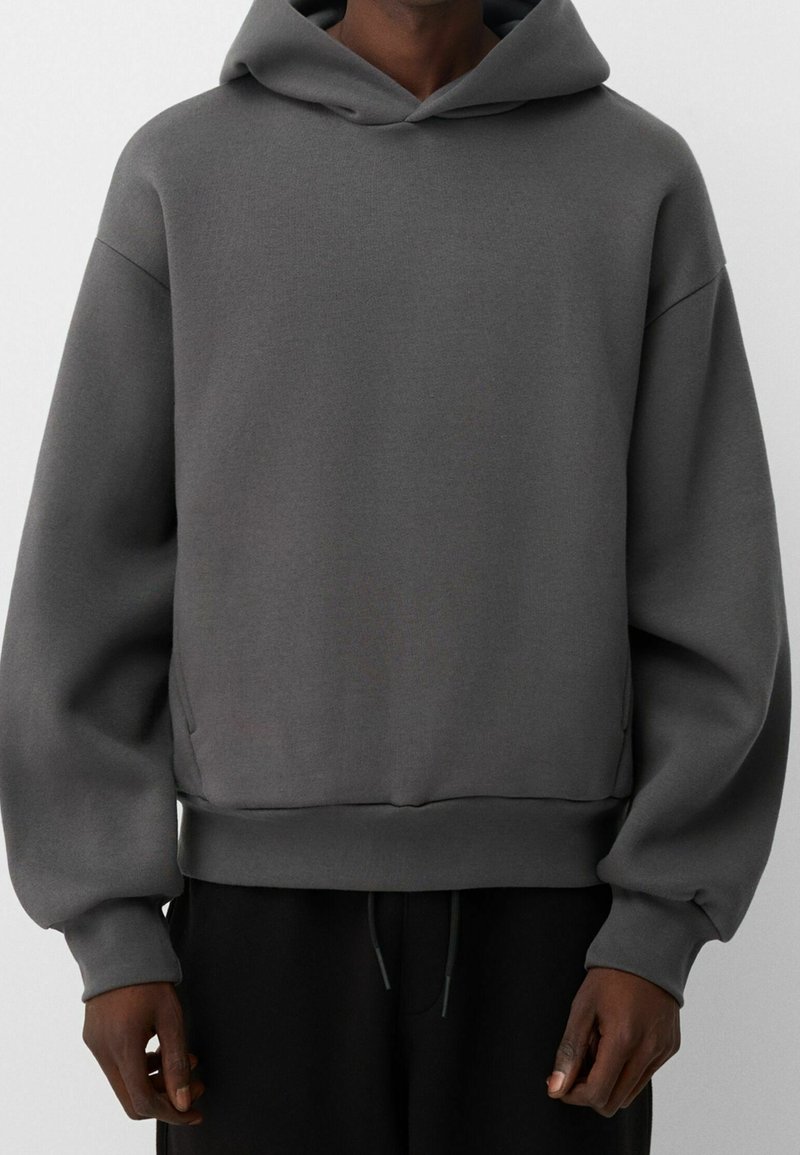 Grå huvtröja med avslappnad passform, tillverkad av mjukt tyg. Har dragsko i huva, vida ärmar och ribbad nederkant och ärmar.