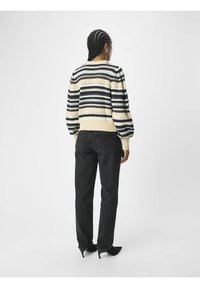 Strikket sweater med horisontale striber i creme, marineblå og mørkegrå. Har en ribbet kant og manchetter. Parret med sorte jeans og høje hæle.