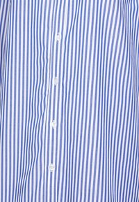 Camicia a righe blu e bianche con righe verticali, dotata di chiusura a bottoni sul davanti e realizzata in tessuto leggero e testurizzato.