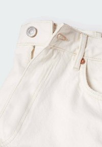 Gros plan sur la ceinture d'un jean en denim blanc cassé, montrant le bouton en métal, la fermeture éclair, la passoire à ceinture et les détails de couture de la poche avant.