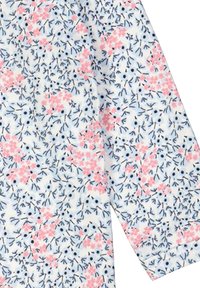 Tkanina s květinovým vzorem se svými růžovými květy a námořnickými stonky na bílém pozadí. Obsahuje dlouhé rukávy s hladkým povrchem.