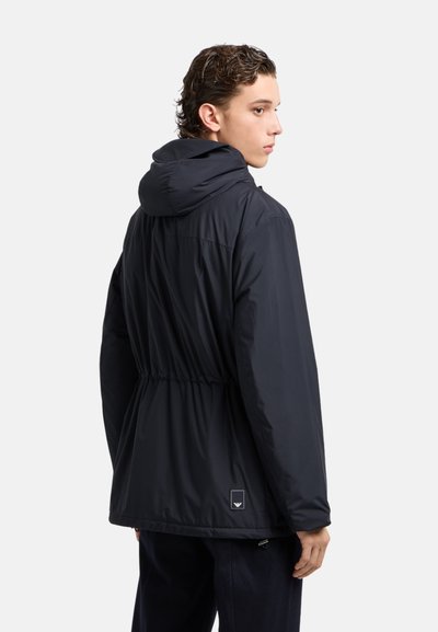 Giacca nera con cappuccio, vita costretta, tessuto liscio e dettaglio con logo sul retro, progettata per una vestibilità rilassata, adatta per un look casual.