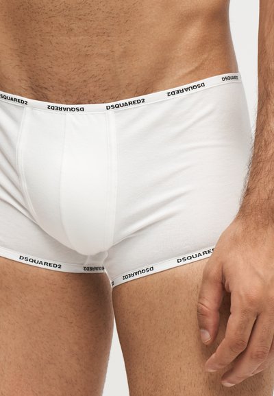 Buste masculin portant un boxer blanc de la marque Dsquared2 avec une ceinture visible et une main latérale reposant près de la cuisse.