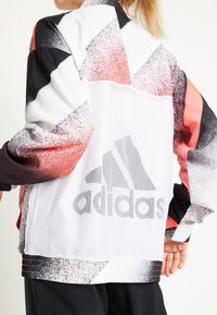Adidas jacket featuring a multicolored geometric pattern in black, white, and red, with a mesh back and large logo on the lower back.