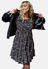 Abito a fiori realizzato in tessuto leggero; sfondo scuro con fiori blu, bianchi e arancioni; bordo a balze a strati sull'orlo.