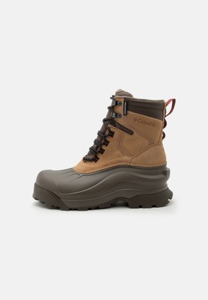 Botte d’hiver imperméable marron et vert foncé avec semelle robuste, lacets noirs et logo Columbia sur le côté.