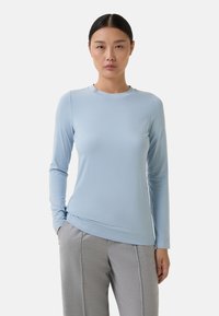 Haut bleu clair à manches longues avec un col rond, texture lisse et design ajusté, associé à un pantalon gris sur mesure.