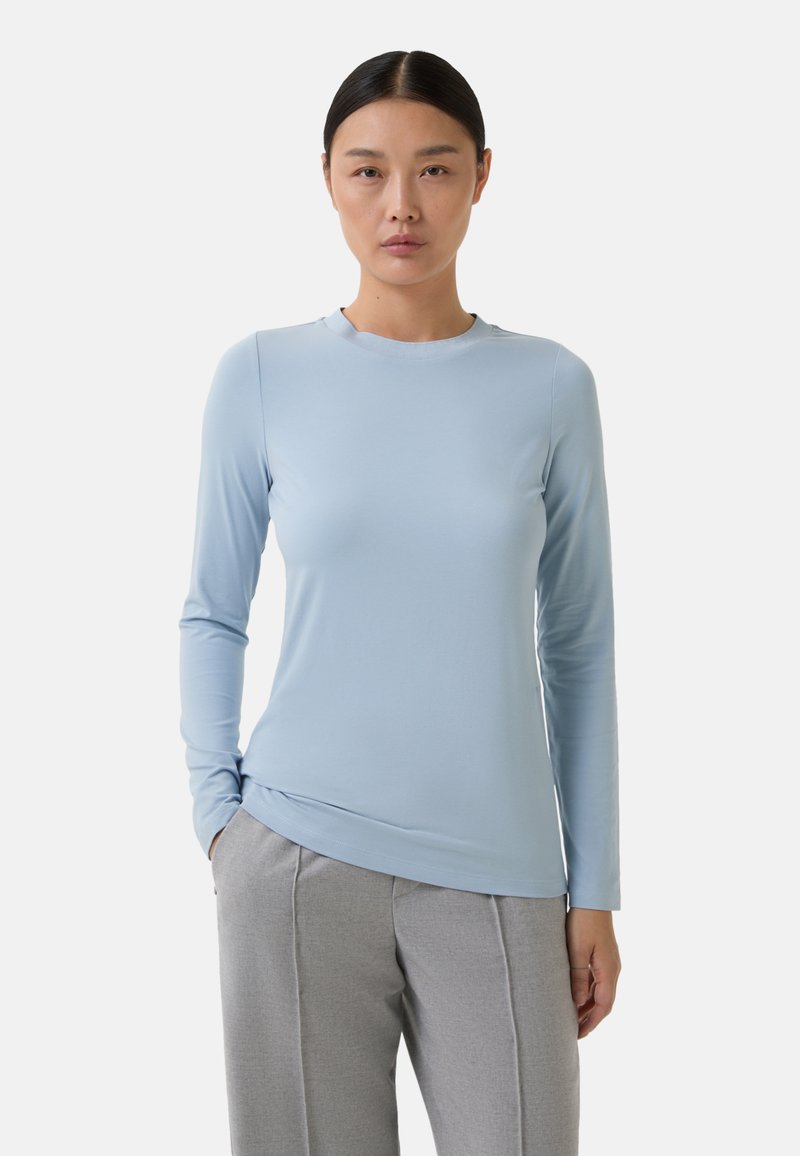 Haut bleu clair à manches longues avec un col rond, texture lisse et design ajusté, associé à un pantalon gris sur mesure.