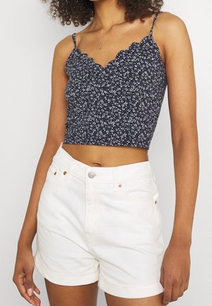 Marineblå blomster crop top med bølget kant og tynde stropper, parret med højtaljede hvide denimshorts med opsmøgede kanter.