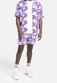 Korte mouwen knop-overhemd en bijpassende shorts in een paars en lavendel abstract patroon. Gemaakt van lichtgewicht stof, gecombineerd met witte sneakers.