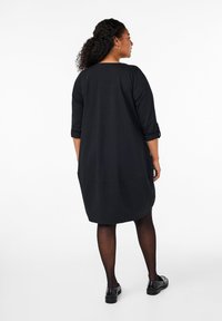 Vestido negro a la altura de la rodilla con mangas de tres cuartos, un ajuste relajado y bolsillos laterales. Presenta una textura suave y lisa y puños de manga enrollados.