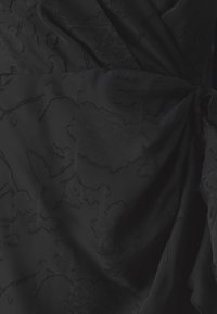 Μαύρο ύφασμα φορέματος με λουλουδάτη υφή και απαλό λαμπερό φινίρισμα. Διαθέτει ρυθούν σχέδιο και μαλακή, λεία επιφάνεια.