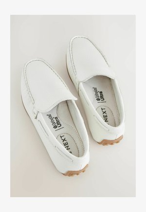 Baskets blanches à enfiler en cuir texturé, avec une pointe arrondie et des coutures minimalistes. La semelle intérieure porte une marque imprimée.